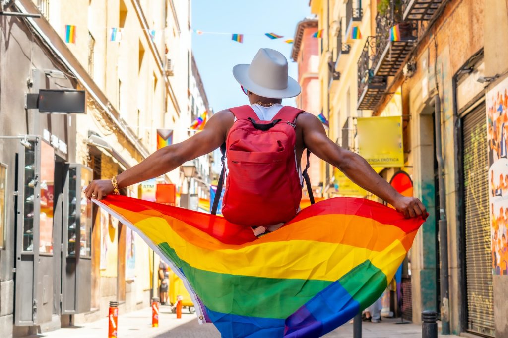 A gay black man walking at the pride party with an LGBT flag, walking backwards