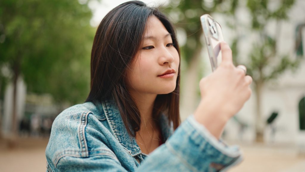 Beautiful Asian woman looking inspired taking photos of beautiful city on smartphone