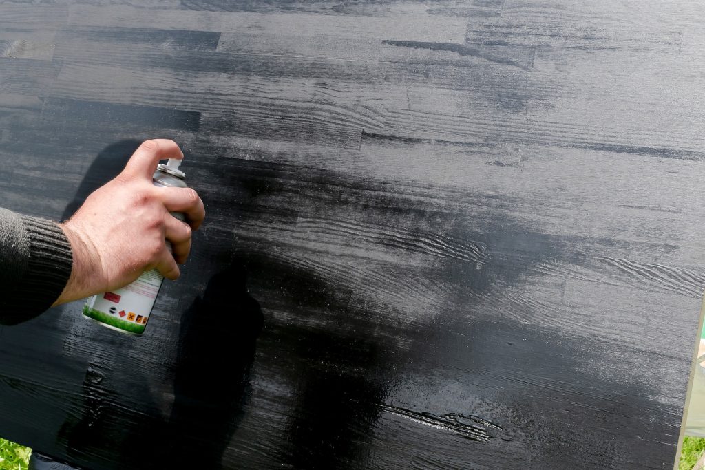 Mans male hand painting wood with black spray paint. Worker applying varnish paint on wooden table