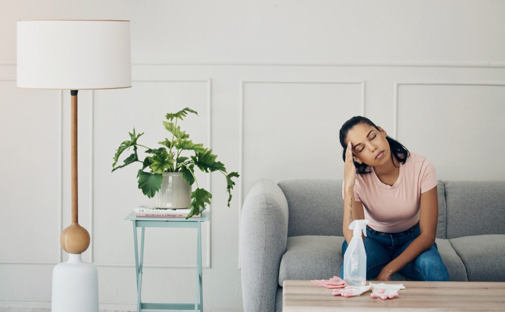 Shot of a woman looking stressed while busy cleaning at home