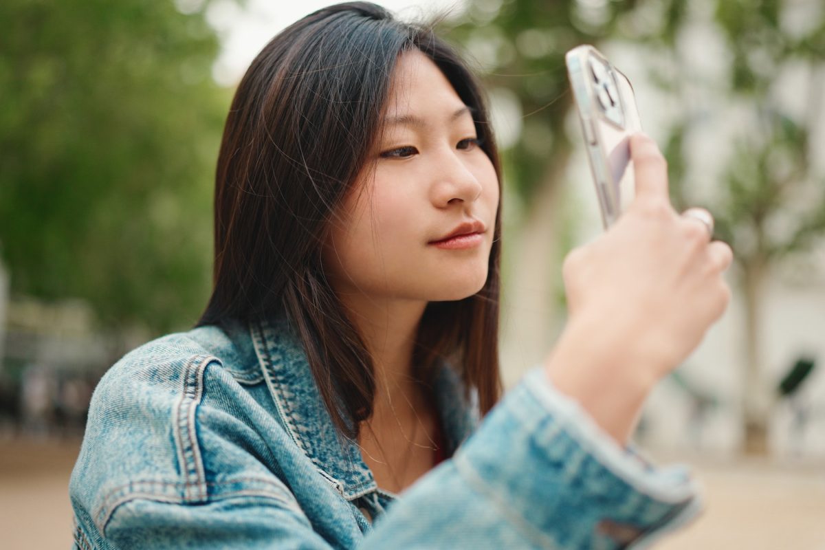 Beautiful Asian woman looking inspired taking photos of beautiful city on smartphone