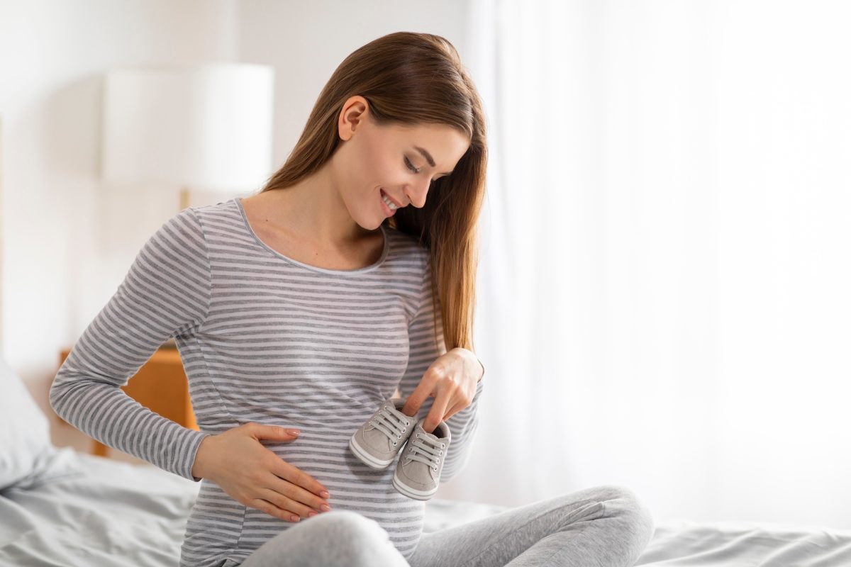 Pregnant lady with baby shoes in bedroom